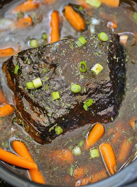 Close-up of a slow-cooked Barbecue Honey Pot Roast with carrots, bathed in rich gravy and garnished with chopped green onions.