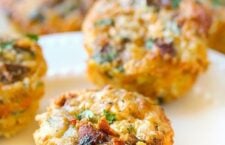 Close-up of a Cheesy Hash Brown and Egg Breakfast Muffin on a white plate, with more muffins in the background.