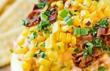 Lip-smacking cheesy bacon and fresh corn dip served in a bowl, accompanied by crunchy crackers - the ultimate snack for flavor enthusiasts.