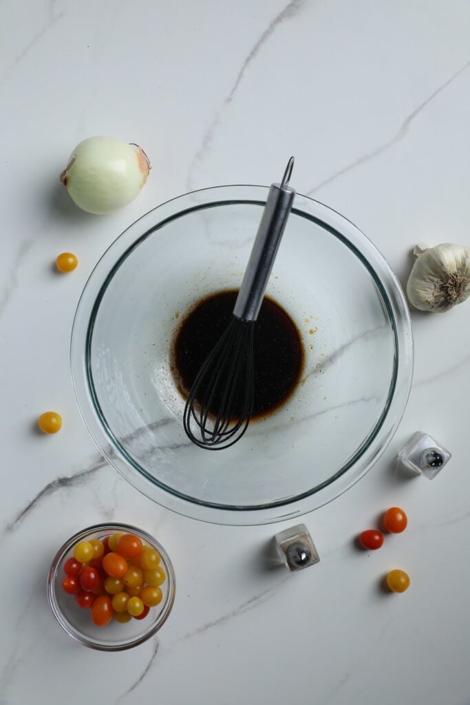 Whisking up the Perfect Marinade for Steak Bites Whisk in a bowl of marinade with fresh vegetables and spices arranged around it, ready for steak bite preparation.