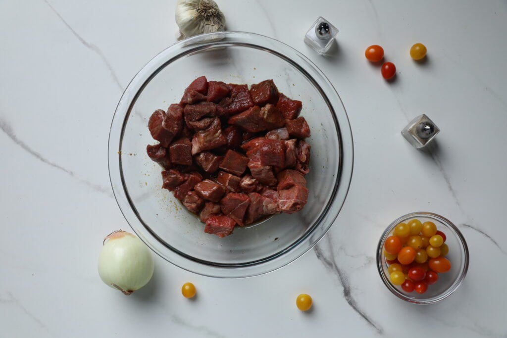 Steak Bites Marinade with Fresh Ingredients Freshly marinated beef cubes with vegetables and spices ready for cooking, laid out on a kitchen surface.
