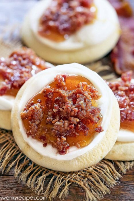 A maple bacon cookie on burlap. The cookie is facing the camera and topped with a candied maple syrup glaze with bacon chunks.