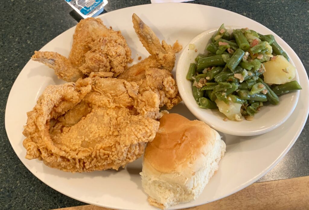 Dixie Chicken and Ribs Plate A hearty meal of golden fried chicken accompanied by a side of vibrant green beans, served on a simple white plate. The chicken, crispy and perfectly browned, contrasts beautifully with the fresh, bright green of the steamed beans, which are lightly seasoned.