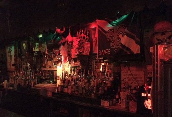20 Must-Try Foods and Activities in New Orleans 23 Inside Aunt Tiki's, the bar display is eclectic and moody, featuring an array of colorful liquor bottles neatly arranged on shelves behind the bar. The shelves are backlit with dim, red lighting, contributing to the bar's gothic and mysterious ambiance.