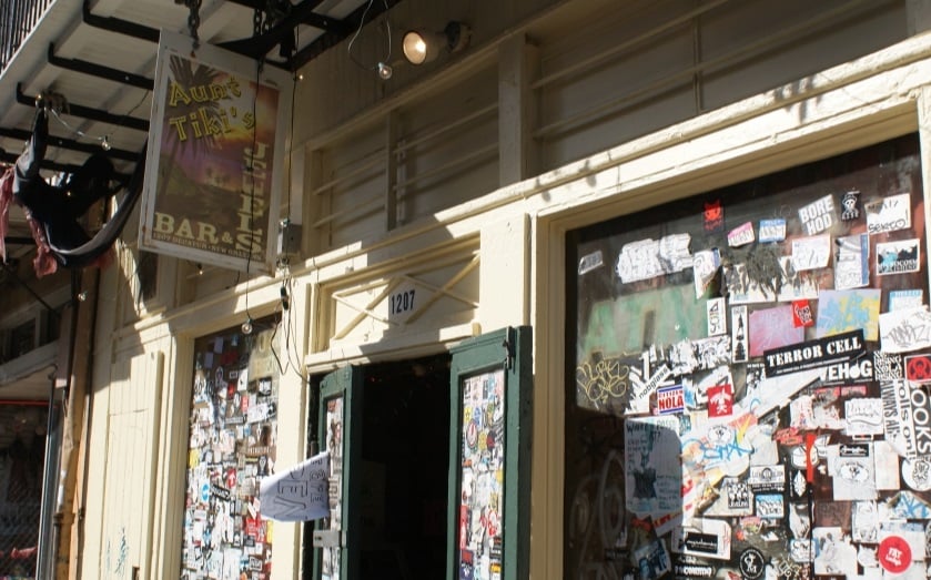 20 Must-Try Foods and Activities in New Orleans 22 The entrance is marked by a faded, vintage sign above the door that reads "Aunt Tiki's" in eerie, stylized font, illuminated by soft, ambient lighting.