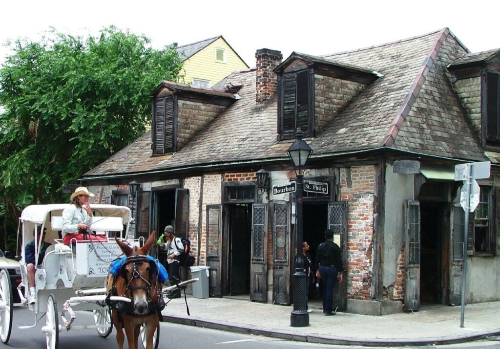 20 Must-Try Foods and Activities in New Orleans 18 Jean Lafitte's Blacksmith Shop, located on Bourbon Street in New Orleans, is portrayed in its charming and rustic glory. This historic building, one of the oldest structures in the French Quarter, features weathered brick and stucco walls, with wooden shutters and a faded, shingle roof that enhances its 18th-century architectural style.
