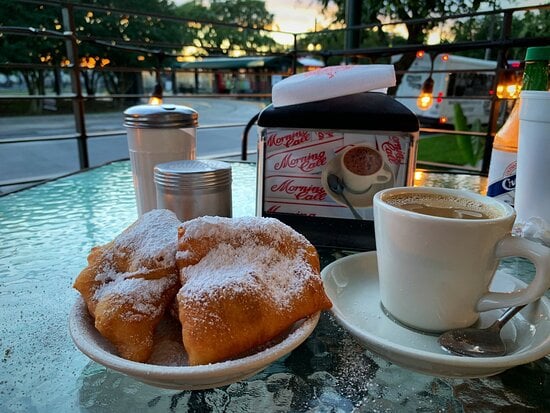 20 Must-Try Foods and Activities in New Orleans 25 An inviting outdoor setting at Morning Call featuring a cup of cafe au lait and a plate of hot beignets, heavily sprinkled with powdered sugar