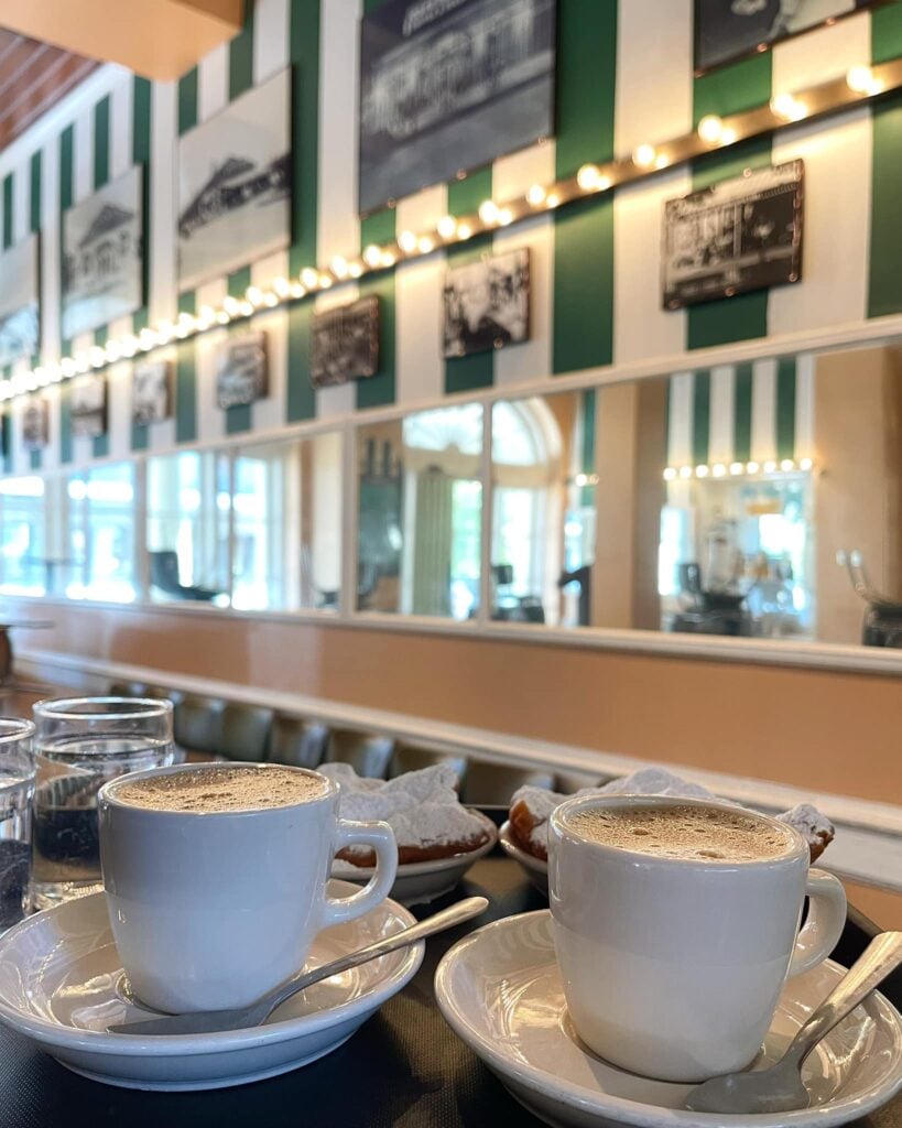 20 Must-Try Foods and Activities in New Orleans 26 A traditional Café du Monde setting featuring a hot café au lait and three freshly-made beignets, generously dusted with powdered sugar.